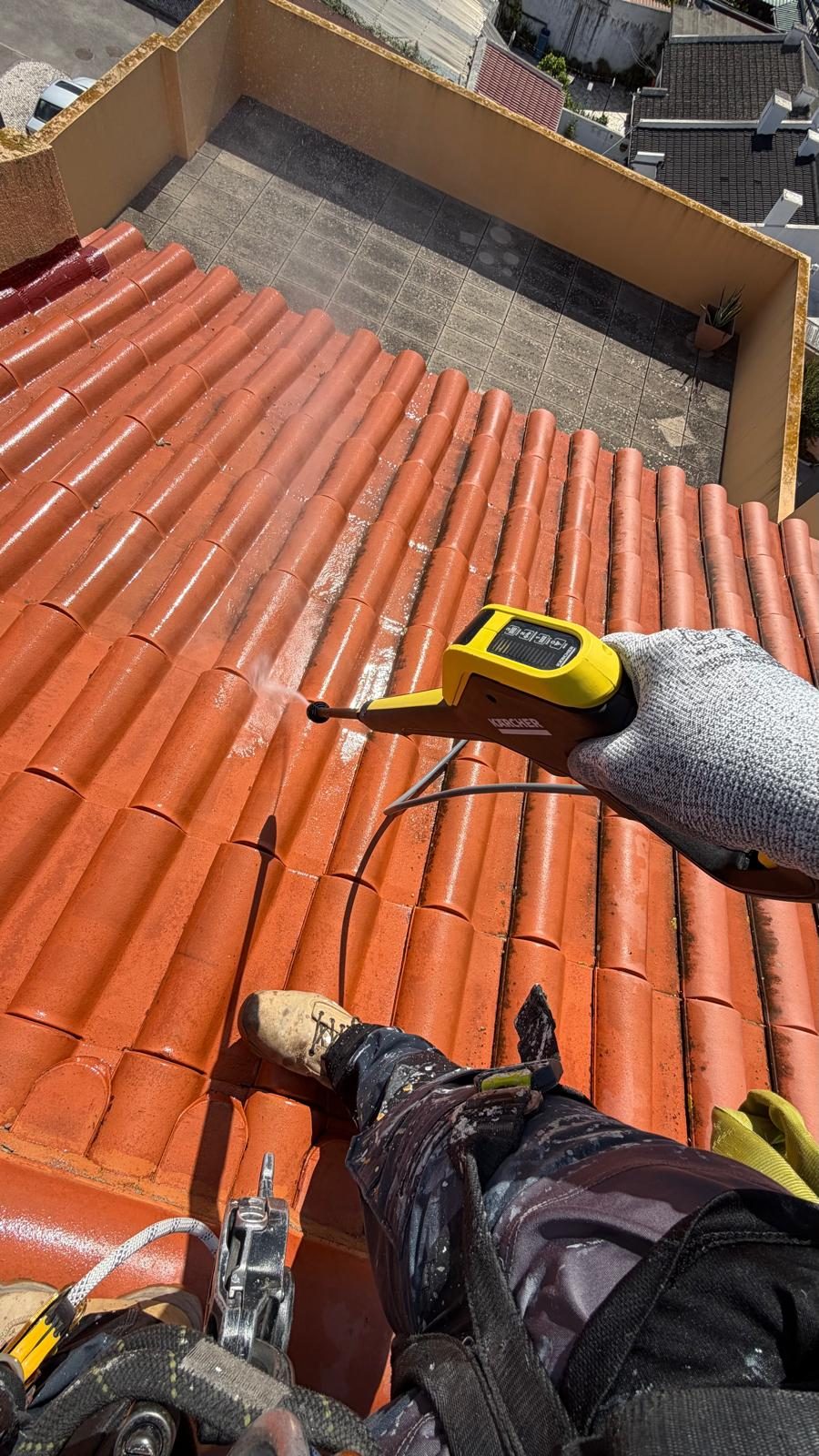 Técnico a lavar a telha com lança de máquina de pressão, visto de cima da cobertura