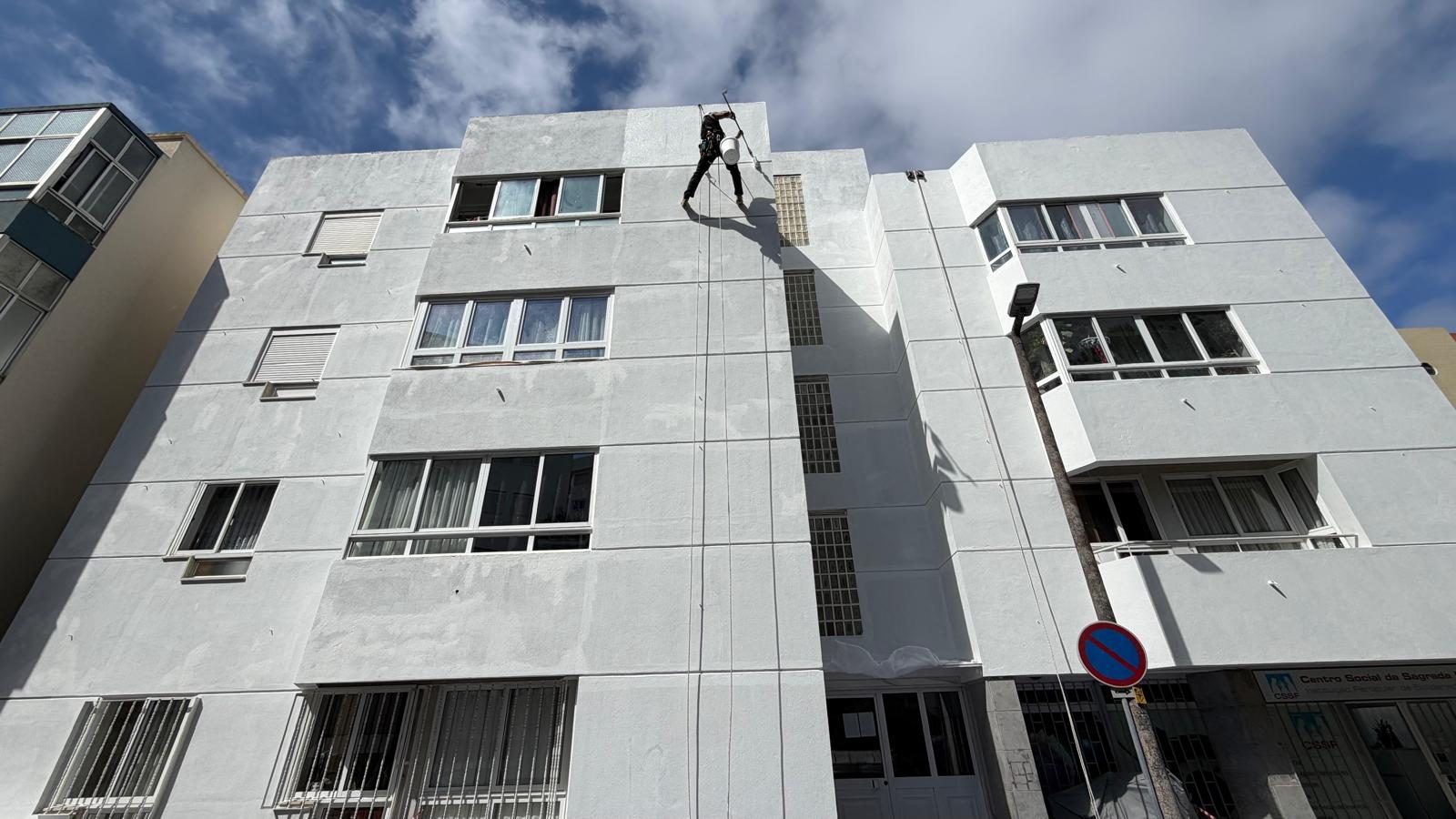Técnico em suspensão a pintar a fachada de um edifício de cinco pisos